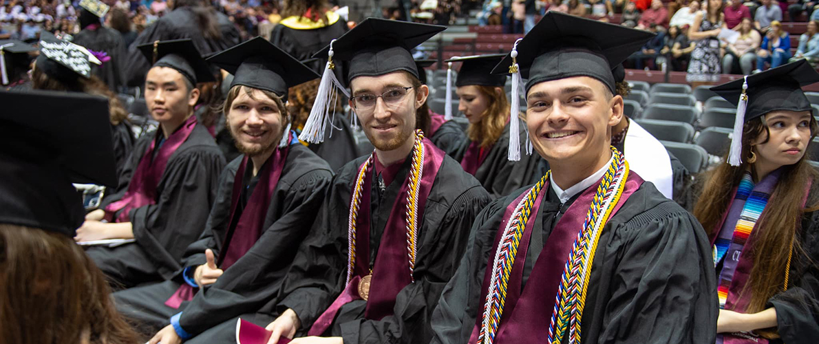 Two young men in graduation regalia smile toward camera